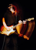 Studio portrait: handsome young man (rock musician) with long hair playing the electric guitar. Blurry (motion) effect