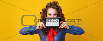 woman on yellow background hiding behind tablet PC blank screen