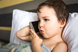 young smart boy talking mobile phone lying on the bed in morning