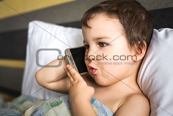 young smart boy talking mobile phone lying on the bed in morning