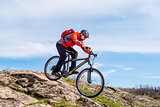 Cyclist in Red Jacket Riding Mountain Bike Down Rocky Hill. Extreme Sport and Adventure Concept.