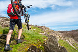 Enduro Cyclist Taking his Mountain Bike up to Beautiful Rocky Trail. Extreme Sport and Adventure Concept.