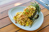 Fried rice in pineapple Thai style in white plate with spoon on the wooden table. Selective focus.