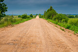 view of a rural dirt road in a field in cloudy weather