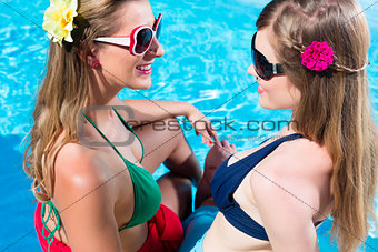 Girl friends tanning at swimming pool in front of water