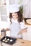 Cooking buns. Girl with tablet in kitchen. Light wooden backgrou