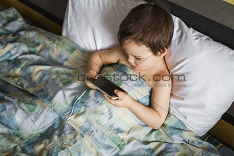 modern boy playing phone lying on the bed in morning