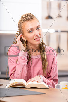 Young smiling woman reading book at table