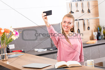 Pretty young woman taking a selfie in the kitchen