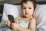 boy holding phone lying on the bed in morning
