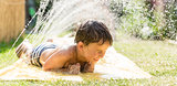 Boy cooling down with garden hose, family in the background