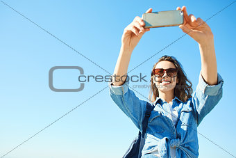 portrait of a young attractive woman using phone on the blue sky background