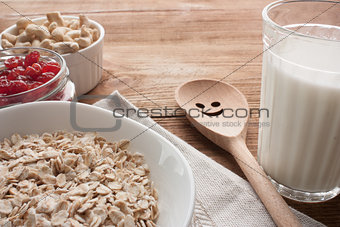 Oatmeal with dried cherries, cashews, milk and a wooden spoon on wooden table.