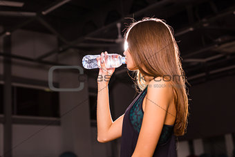 Fitness young woman drinking water in the gym. Muscular woman taking break after exercise