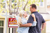 Caucasian Couple Facing and Pointing to Front of Sold Real Estat