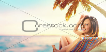 Beautiful girl sitting on a deck chair at the beach at sunset