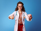 paediatrist woman with piggy bank showing thumbs up on blue