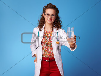 smiling pediatrist woman giving glass of water on blue