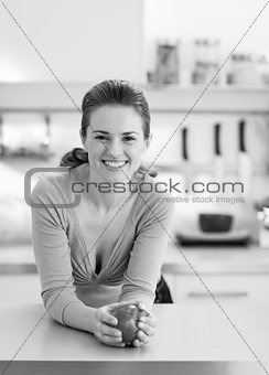 Portrait of happy young housewife with apple in modern kitchen