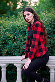 City fashion: portrait of beautiful young girl wearing checkered shirt and jeans in park among green plants