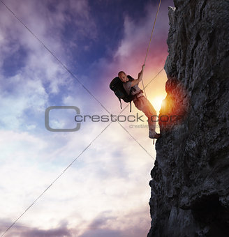 Man climbs a high danger mountain with a rope during sunset