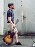 Bearded man walking with acoustic guitar
