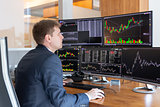 Stock trader looking at computer screens in trdading office.