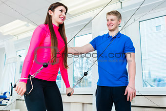 Athlete using workout equipment in gym and getting assistance by trainer