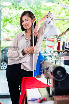 Asian tainlor or fashion designer leans on sewing desk