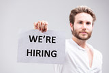 Bearded man holding up a We're Hiring sign