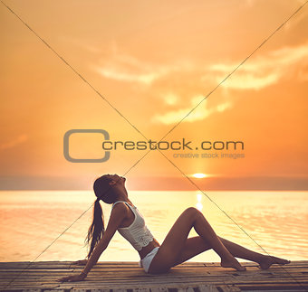 beautiful sexual woman in white bikini on a wooden pier against the sea and sunset