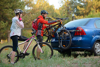 Young Couple Unmounting Mountain Bikes from Bike Rack on the Car. Adventure and Family Travel Concept.