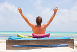 Relaxed man in luxury lounger, arms rised, enjoying summer vacations on beautiful beach.
