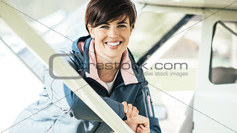 Young smiling female pilot leaning on a plane
