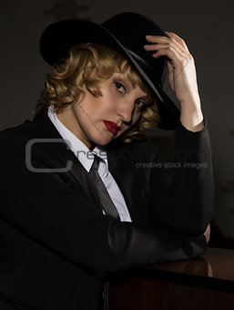 Elegant woman in business suit with a hat poses on a dark background, stylized retro portrait