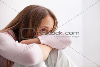 Sad teenager girl sitting on the floor propping head on her knee