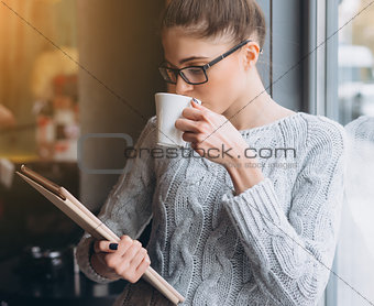 Young girl looking at tablet and smiling in cafe with big window.