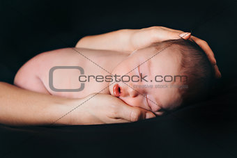 newborn baby lying on the hands of parents on a black background. Imitation of a baby in the womb.
