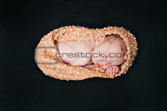 A little child in a beige diaper lies on a black background