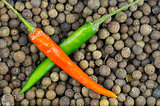 two peppers green and red pod cross hair on a background of large peppercorn  allspice