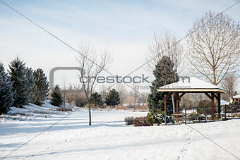 Snow-covered park with trees and gazebo in winter