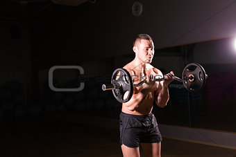 Powerful bodybuilder doing the exercises with barbell. Strong male with naked torso on dark background. Strength and motivation.