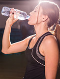 Fitness young woman drinking water from bottle. Muscular young female at gym taking a break from workout.