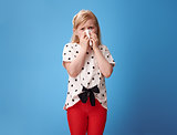 unhappy modern child in red pants on blue blowing nose