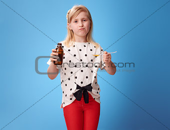 sad modern girl taking spoon of children's suspension on blue