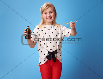 smiling girl giving spoon of children's suspension on blue