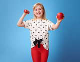 smiling modern girl showing biceps and an apple on blue