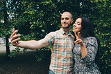 A guy with a girl taking selfies on a green foliage background