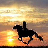 Black silhouette of a woman riding a horse at sunrise