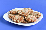 Oatmeal cookies with sesame seeds in a white dish on a violet ba